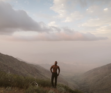 man standing on mountain peak under white clouds