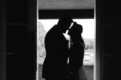 Silhouette of a couple standing closely together in a doorway, with a bright outdoors visible in the background, creating a romantic and intimate scene.
