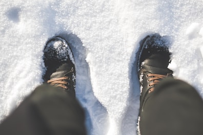 Pair of insulated boots dusted lightly with fresh snow on wooden doorstep