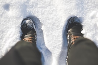 Pair of insulated boots dusted lightly with fresh snow on wooden doorstep