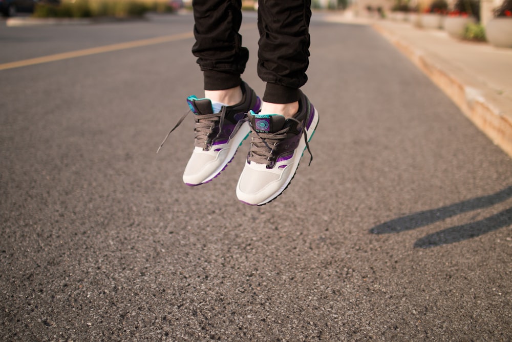 person wearing white and gray sneakers jumping over gray roadway