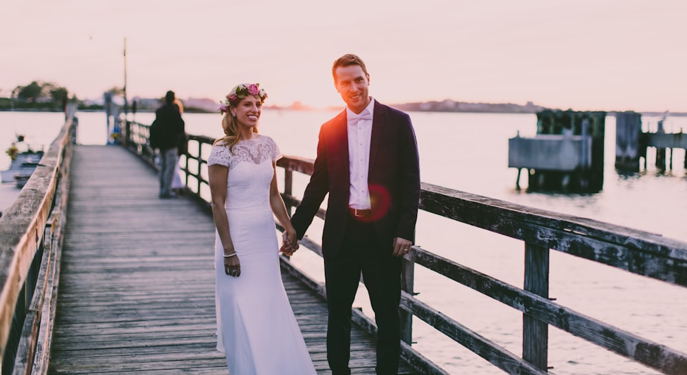 bride and groom standing on wooden dock near body of water