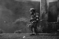 grayscale photography of firefighter holding equipment near houses