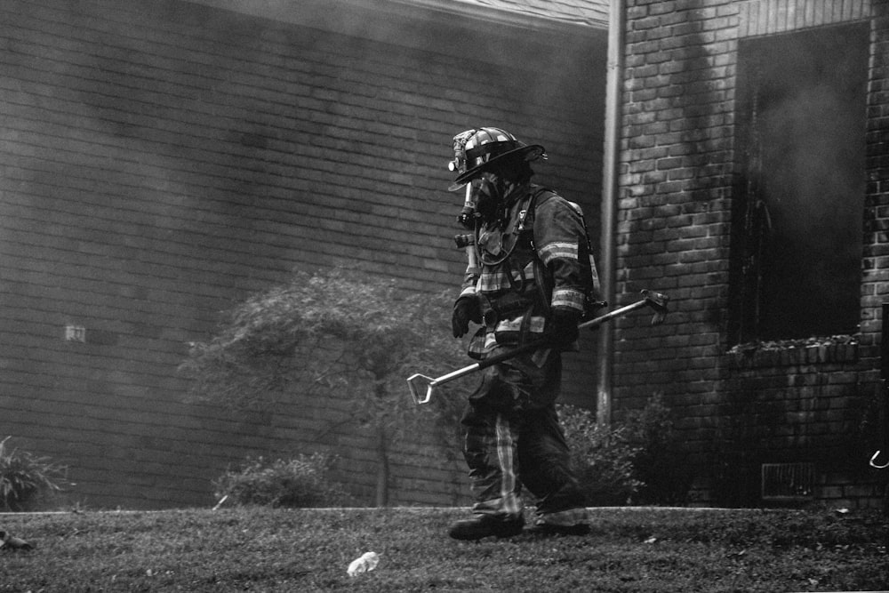 Photographie en niveaux de gris d’un pompier tenant de l’équipement près des maisons