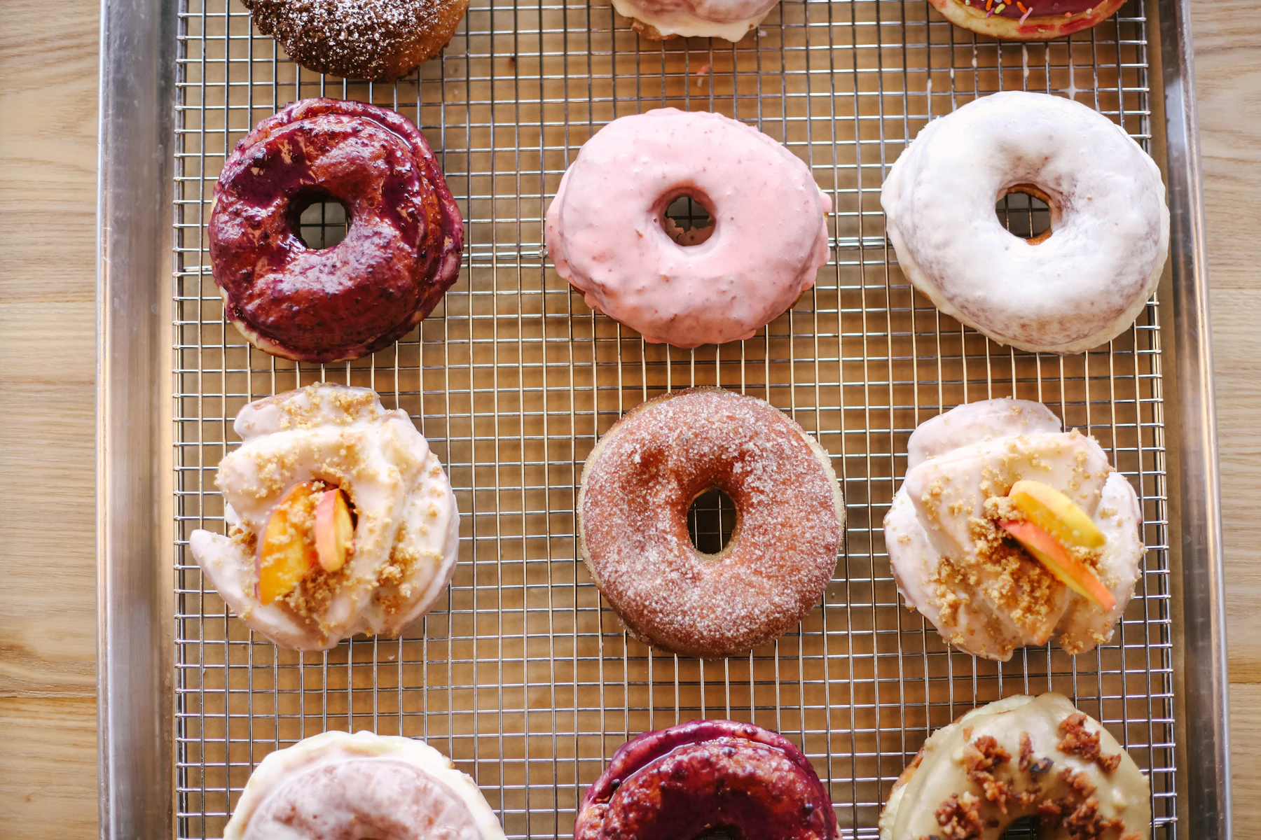 Overhead view of glazed, cinnamon-sugar and berry-iced ring donuts on a wire rack in a sheet pan