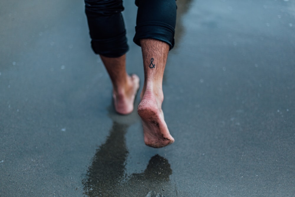pessoa com tatuagem a pé andando em areias molhadas