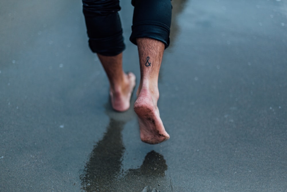 Person mit Tätowierung zu Fuß, die auf nassem Sand geht