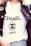 A person is wearing a white T-shirt with the word CHANEL and the logo prominently displayed in black text. A dark denim jacket with an embroidered patch on the shoulder is layered over the T-shirt.