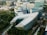 An aerial view of a modern urban area featuring several large, uniquely designed buildings surrounded by lush greenery. The central building has a distinctive, angular shape with a roof partially covered in solar panels. Additional structures with curved designs and glass facades are visible in the vicinity, forming a cohesive architectural setting.