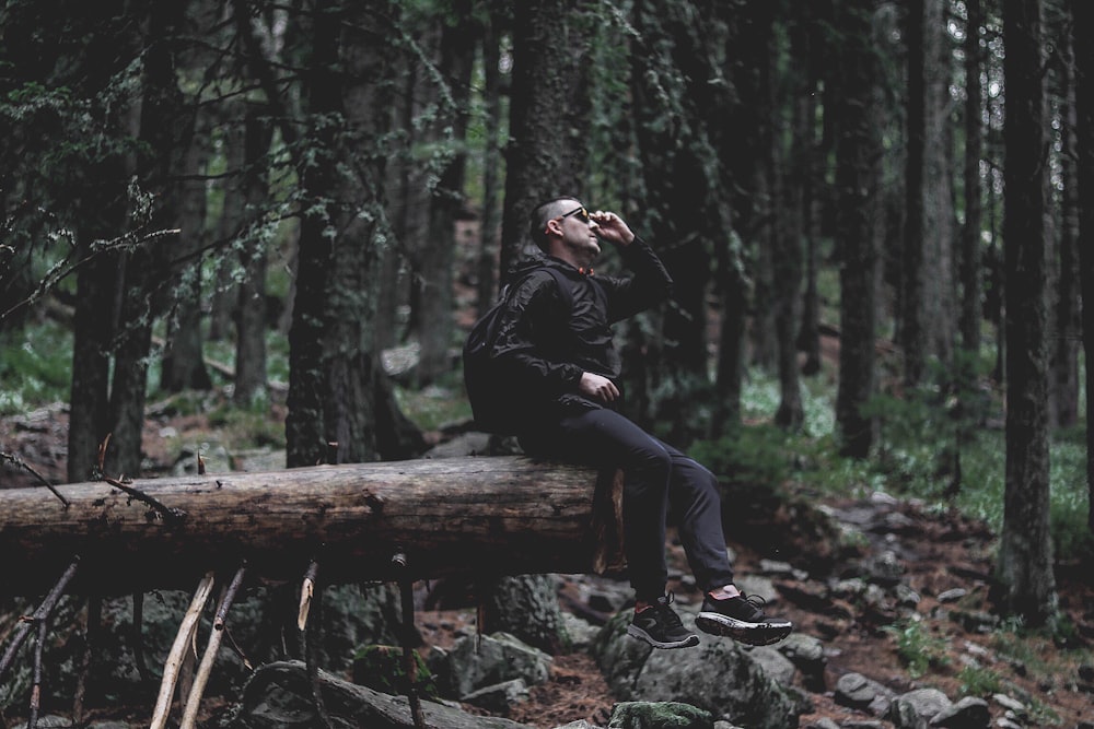 person wearing black jacket on log wod inside the forest