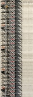 An industrial structure with a scaffolding system against a large concrete wall. The scaffolding features metal beams, platforms, and red sections, casting intricate shadows onto the wall. The concrete surface is smooth with subtle vertical lines.