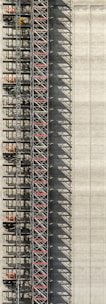 An industrial structure with a scaffolding system against a large concrete wall. The scaffolding features metal beams, platforms, and red sections, casting intricate shadows onto the wall. The concrete surface is smooth with subtle vertical lines.