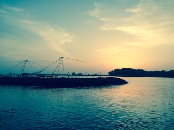 A serene coastal village at sunset with local fishermen casting nets, framed by lush greenery and calm waters.