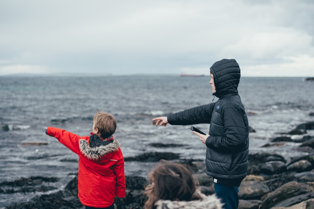 boy and man pointing on sea taken under white clouds during daytime