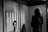 A person stands in an exhibition space, viewing a black and white photograph of an individual in front of a backdrop featuring the American flag. The space around them is dimly lit, focusing attention on both the observer and the photograph.