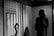 A person stands in an exhibition space, viewing a black and white photograph of an individual in front of a backdrop featuring the American flag. The space around them is dimly lit, focusing attention on both the observer and the photograph.