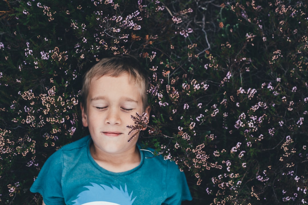 boy on teal shirt lying on pink flowers