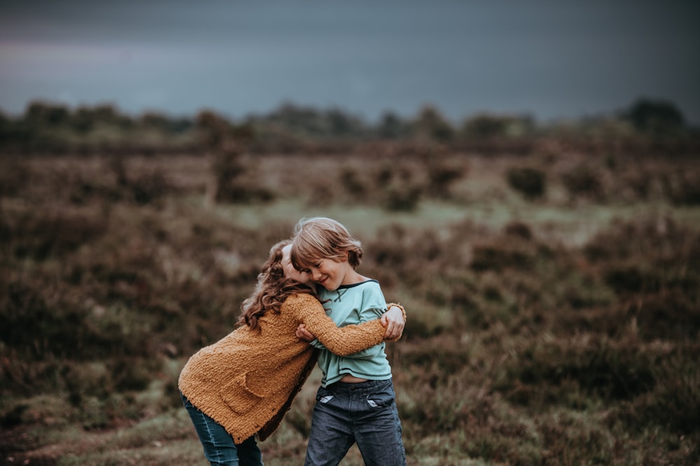 two child hugging in front of field