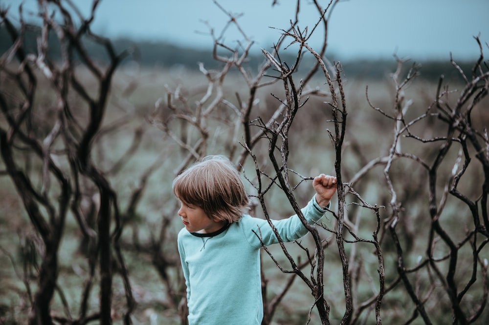 boy wearing teal long-sleeved shirt beside leafless tree