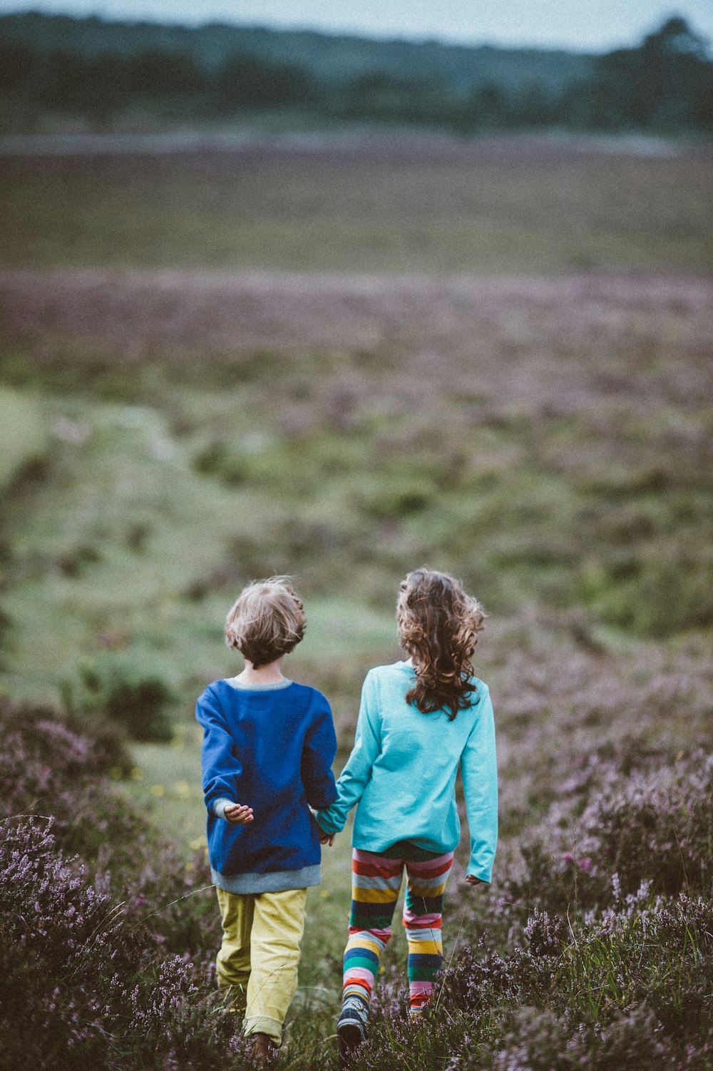 boy and girl holding each others hand while walking on field