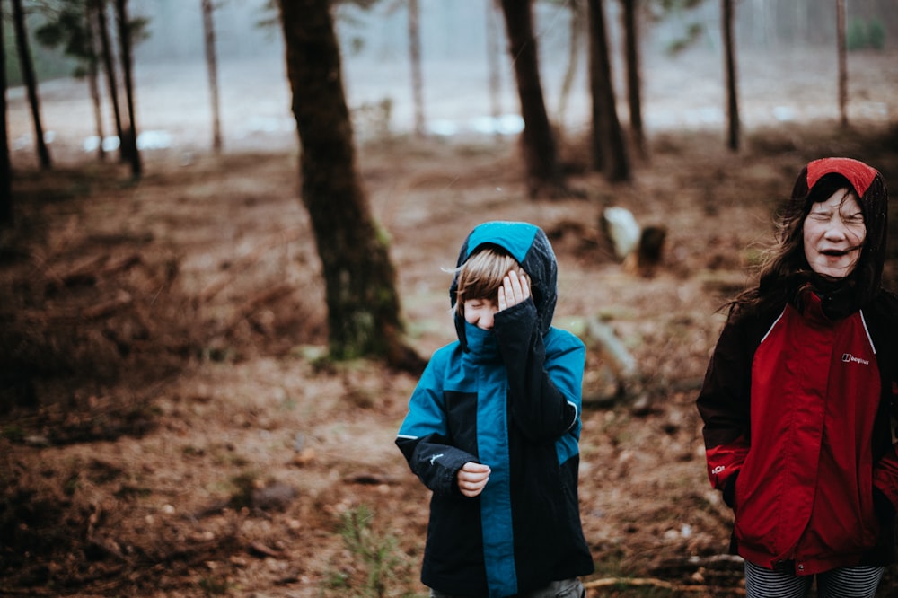 青と赤のコートを着た2人の子供が森の上に立つ