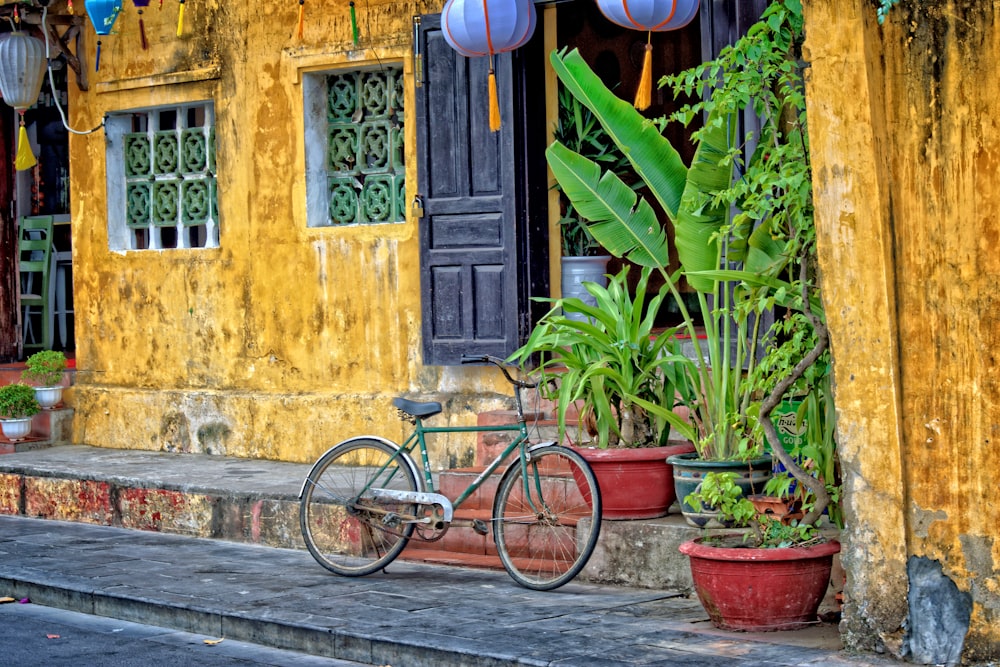 Bicicleta verde estacionada ao lado de casa de concreto amarelo durante o dia