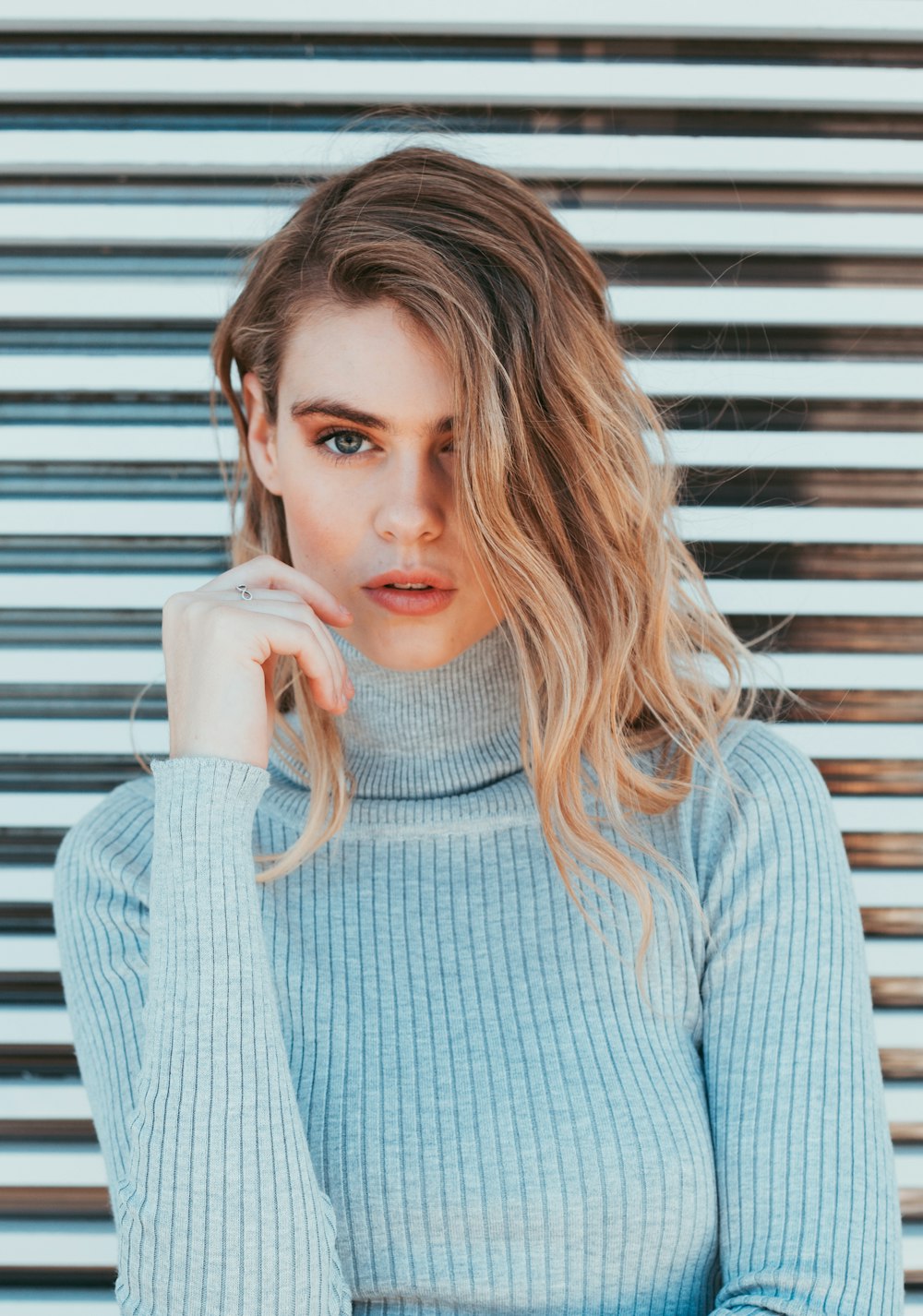 woman wearing gray turtle-neck top standing near white wall