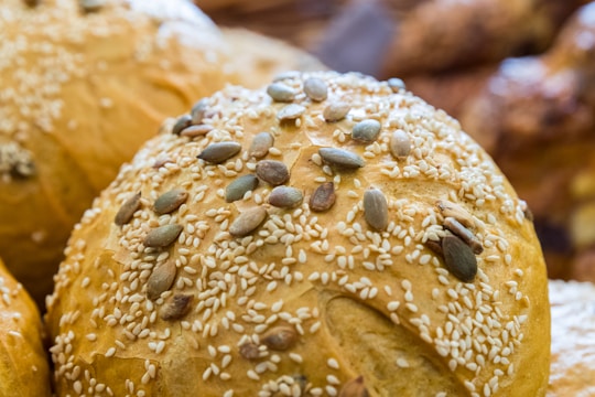 A close-up view of freshly baked bread rolls, topped with a generous amount of sesame and pumpkin seeds. The rolls have a golden brown crust and appear appetizing with a soft texture.