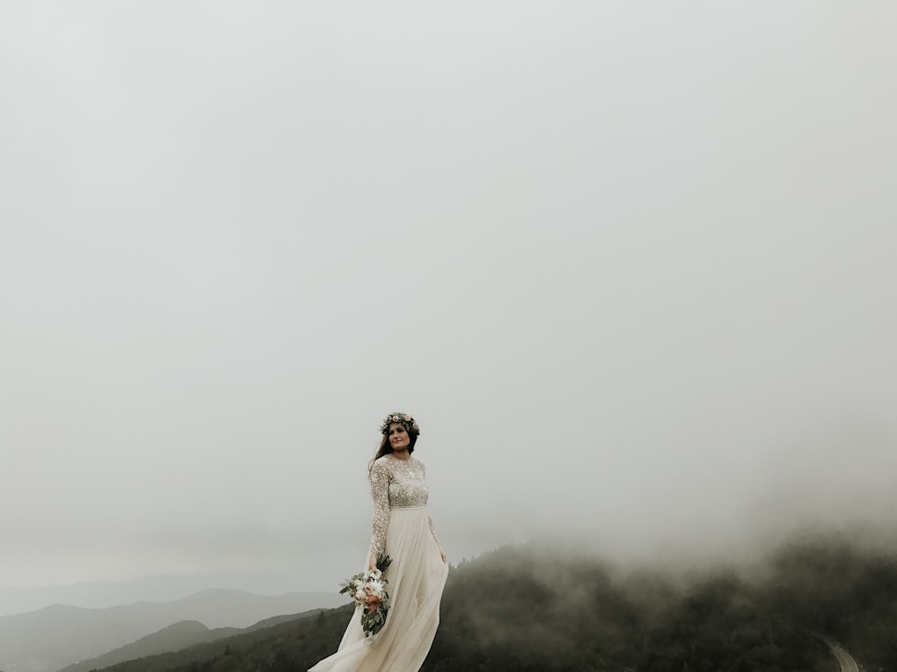 Frau im Hochzeitskleid steht auf dem Gipfel des Hügels