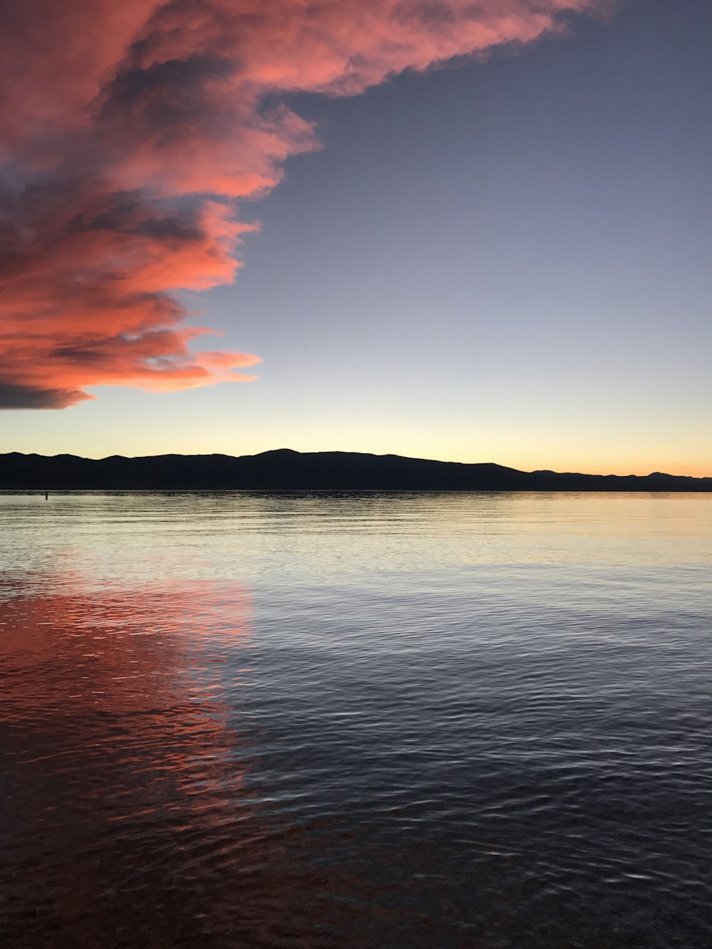 silhouette of hill surrounded by body of water under pink clouds