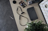 A tabletop with various items including a handheld gaming device, a pair of wired earphones, a plant, a camera lens cap, and a collection of game cartridges in a holder. There are also some stickers featuring colorful designs and characters.