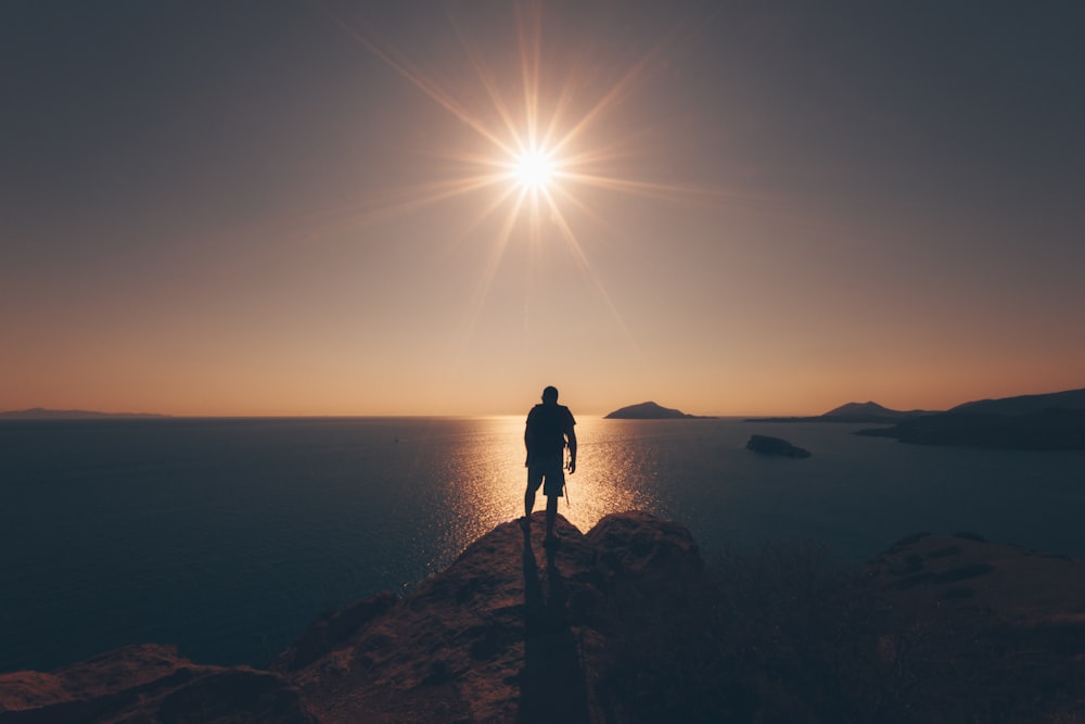 person standing on rock facing sea taken during golden hour