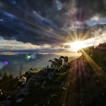 sun rays peak through clouds over herd of goats on hill