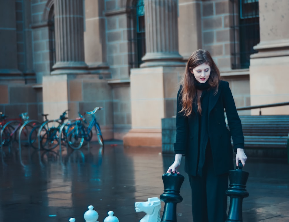 woman in black suit and pants standing near concrete pillar and bikes