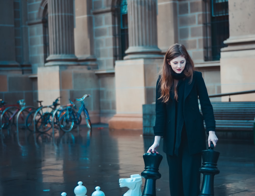 Donna in abito nero e pantaloni in piedi vicino a pilastro e biciclette di cemento
