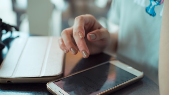A close-up of a hand reaching for a smartphone on a wooden desk.