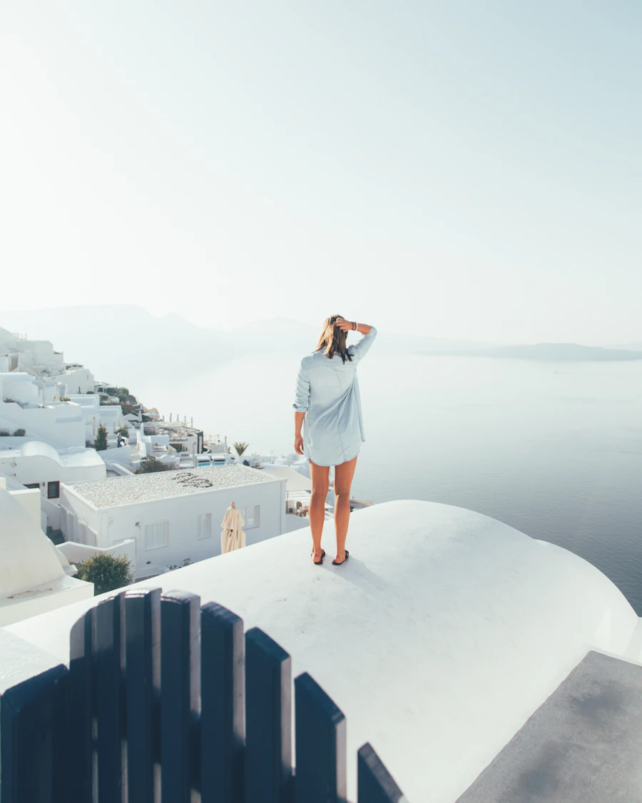 A traveller in white standing on a whitewashed terrace above a misty sea