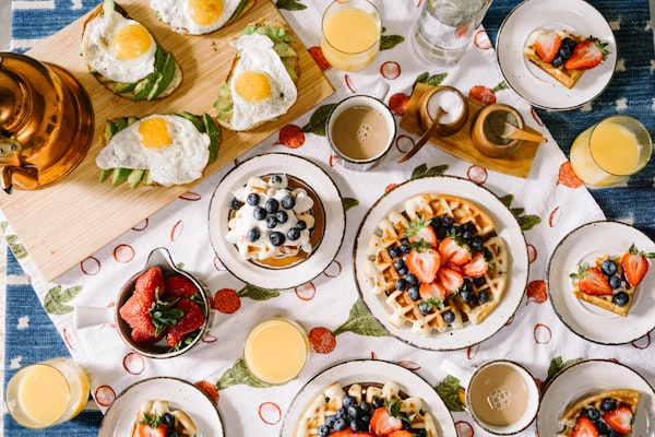 Table de petit-déjeuner avec des assiettes blanches remplies de gaufres, de fruits, d'oeufs, de jus de fruits et de café