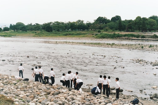 A group of anglers planting native water plants along a riverbank in military green jackets.