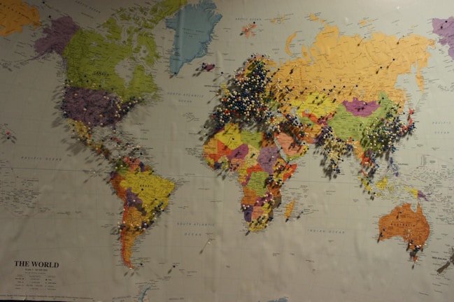 A world map with a multitude of colored push pins inserted into various locations across all continents, densely clustered in parts of Europe, Asia, and North America. The map features country names, borders, and geographical details in different colors for each country. The push pins appear to represent places of interest or significance.