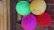 Colorful clown performing tricks with balloons while kids watch excitedly in a white and blue decorated room.