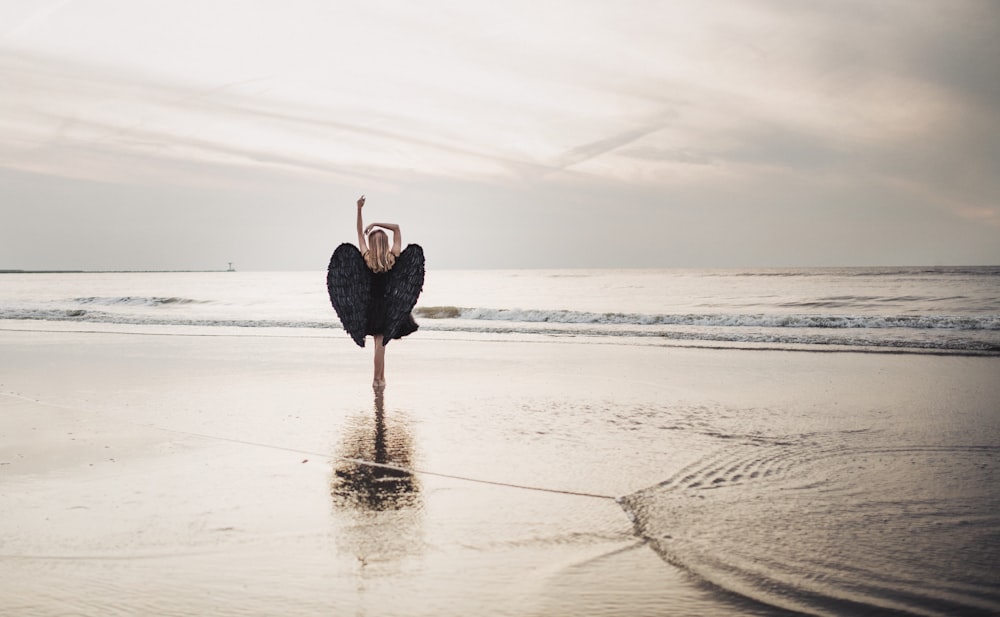 person wearing black wing costume standing on seashore during daytime