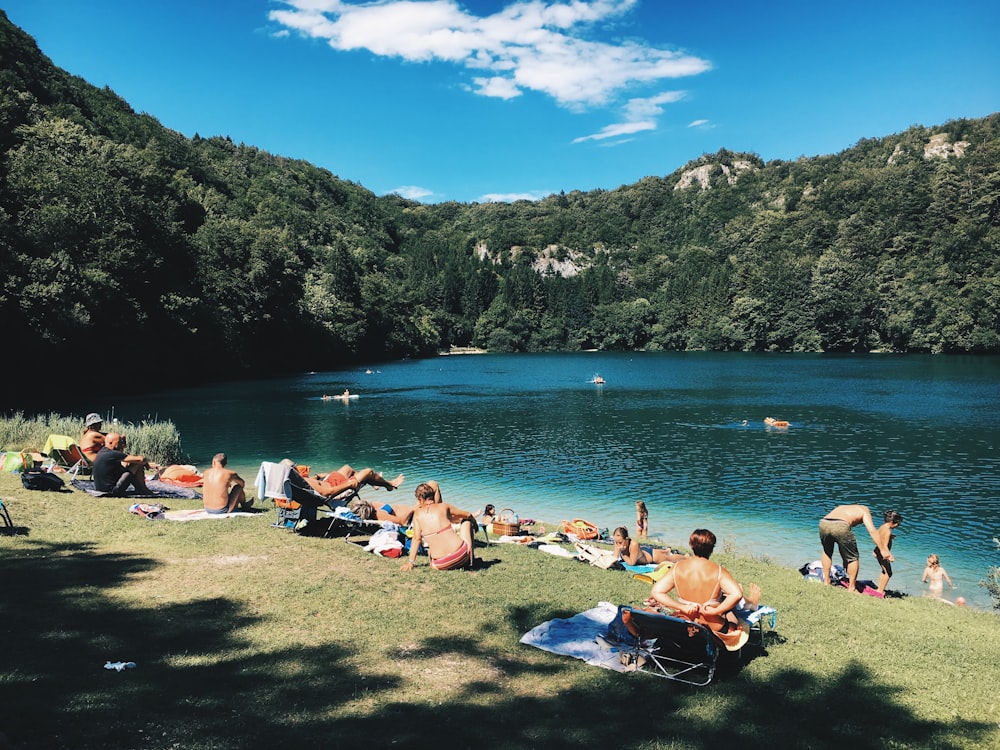 grupo de pessoas reunidas perto do lago sob o céu azul durante o dia