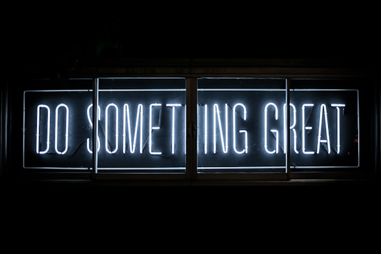 Bright neon sign displaying the words 'DO SOMETHING GREAT' in a bold, white font against a dark background. The sign is framed in a rectangular shape with clear lines, creating a striking contrast.