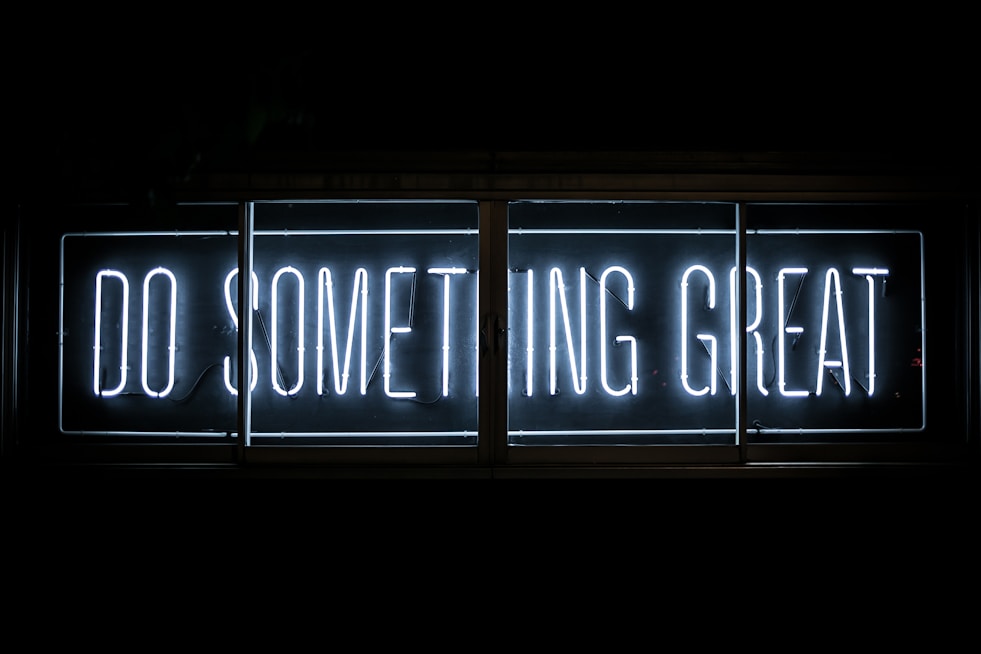 Bright neon sign displaying the words 'DO SOMETHING GREAT' in a bold, white font against a dark background. The sign is framed in a rectangular shape with clear lines, creating a striking contrast.