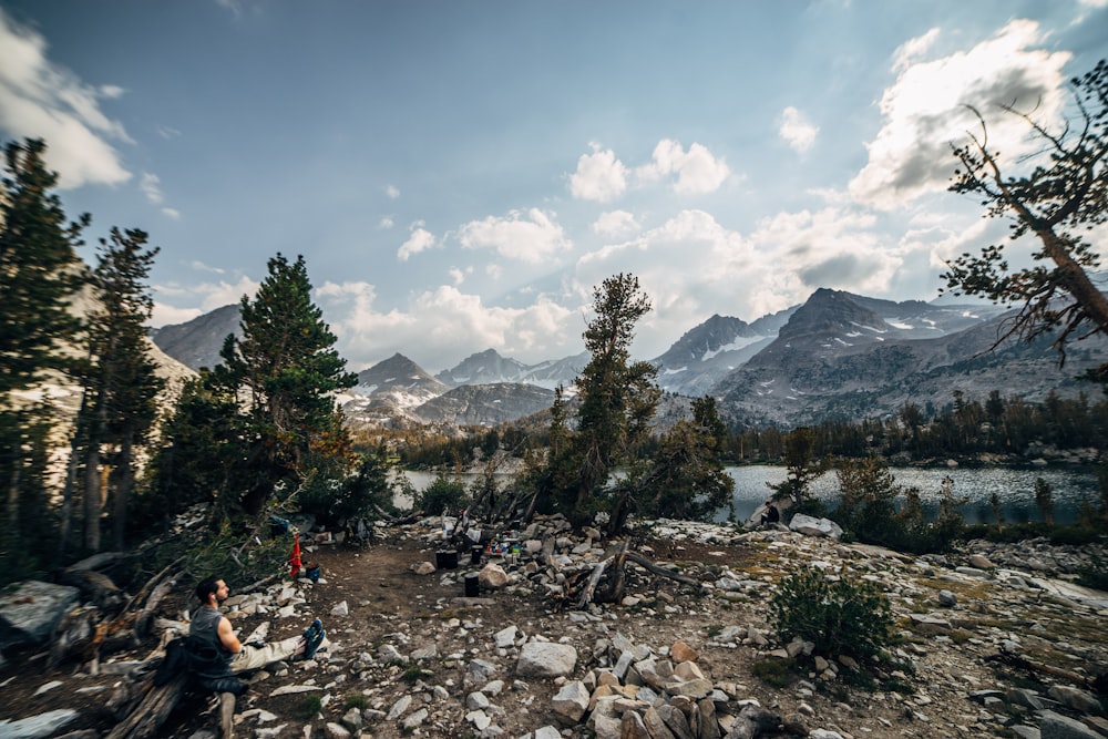 hombre sentado en el suelo frente a las montañas y el lago
