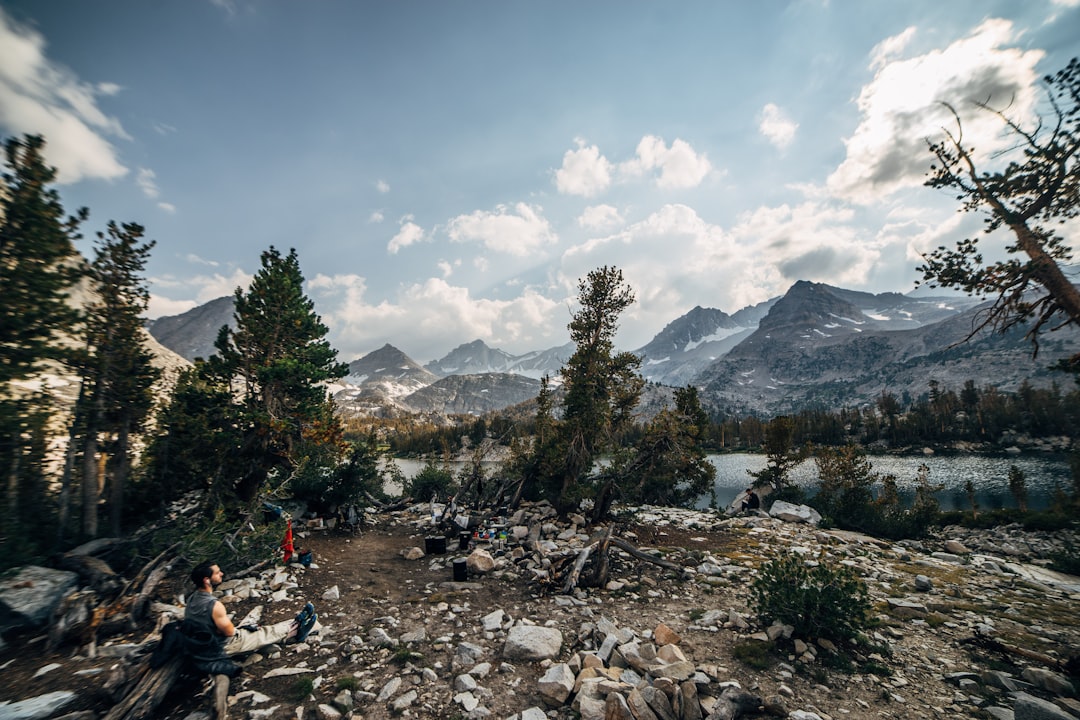 man sitting on ground in front of mountains and lake,