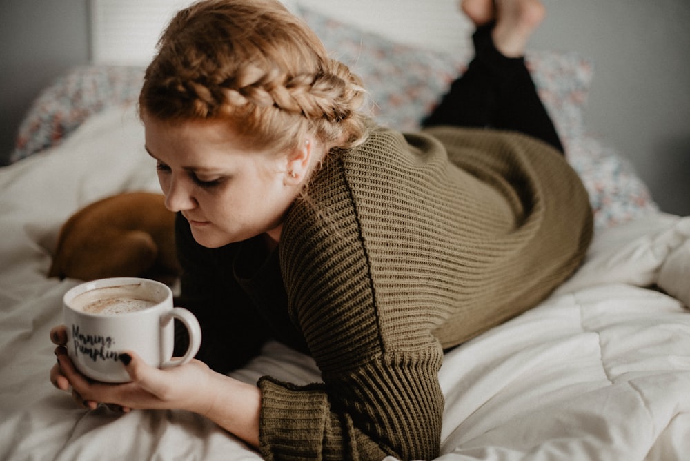 Mujer en la cama sosteniendo una taza blanca