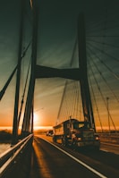 Dwal carrier truck crossing a bridge over a wide river during sunset
