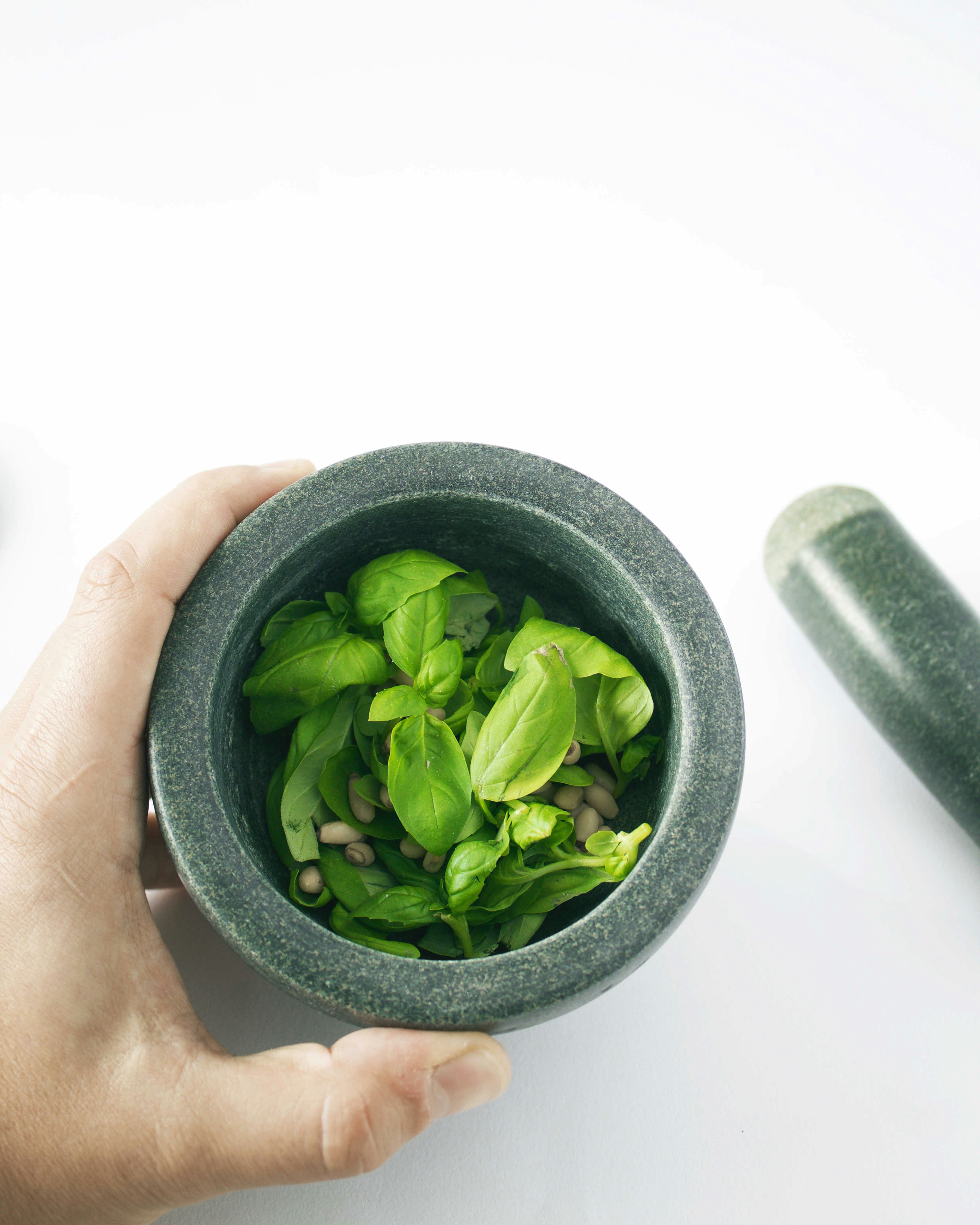 Close-up of hands pinching a basil flower bud from a stem, with a mortar and pestle visible in the soft background